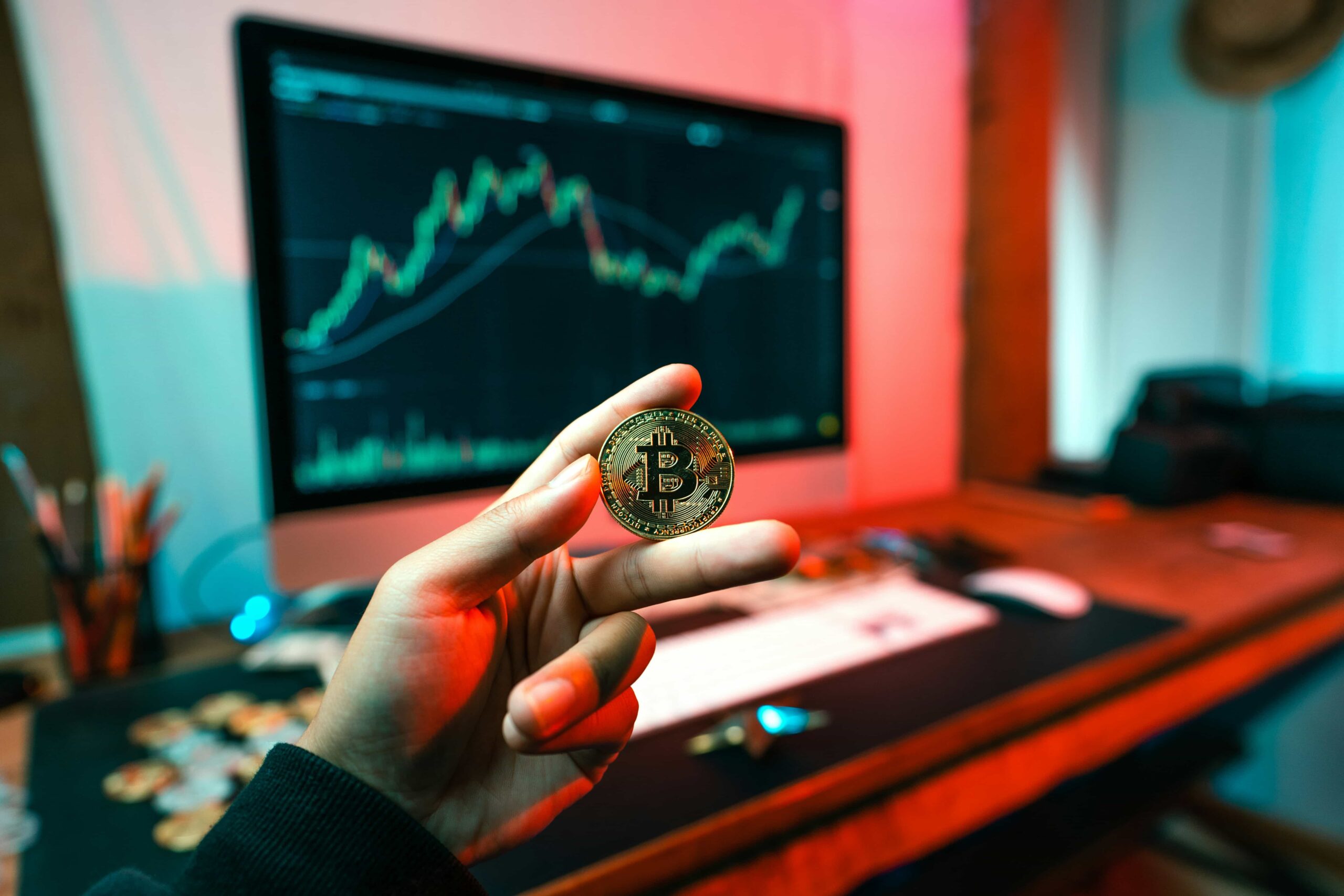 Image of someone holding a bitcoin (commemorative coin) with a stock chart behind it.