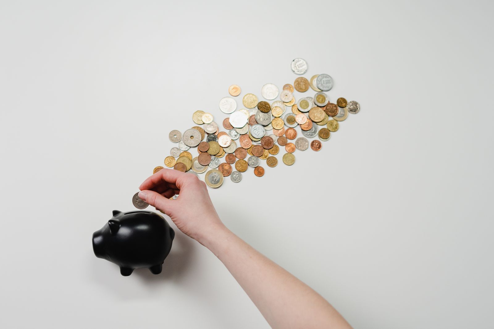 Person placing a coin into a black piggy bank with coins on the table